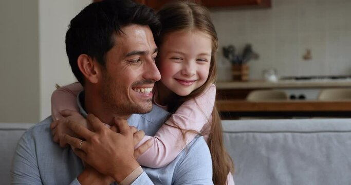 Caring handsome dad enjoy moments of tenderness with little daughter. Cute preschool girl piggyback young loving daddy sit together on sofa spend leisure at home. Family bond, happy father day concept