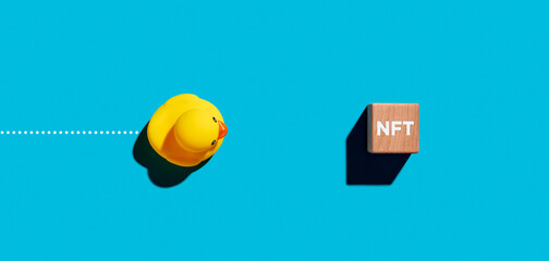 Toy robber duck moves towards a wooden cube with the acronym NFT for non fungible token...