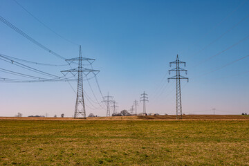 Beautiful farm landscape and high voltage power lines in Germany, at Spring during sunset with blue sky. Concept of energy supply and energy crisis.