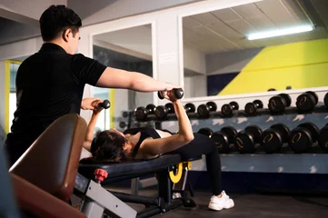 Türaufkleber Image of an attractive woman working out with a personal trainer at a gym in Asia. © somchai20162516