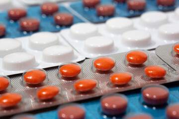 Medicine tablets of different colors are arranged in an orderly manner. Orange colored round pills in selective focus.
