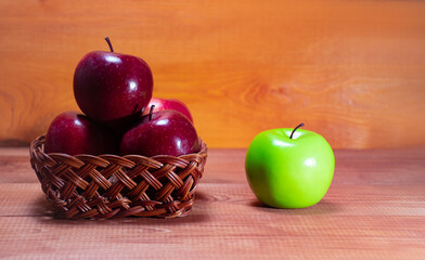 Fresh red apples lie in a wooden basket on a wooden background near one green apple with a place for the text: healthy snack, vitamins, healthy food, ingredients for baking recipes, side view