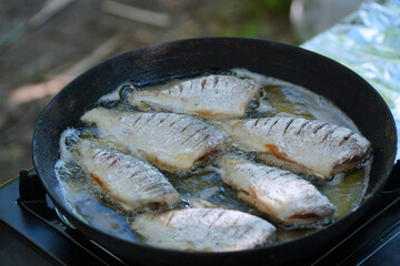 A small river fish rolled in flour is fried in oil in a frying pan