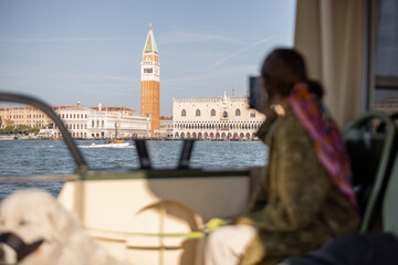 Woman in medical mask sitting in Vaporetto, famous water transportation in Venice. Taking photo of...