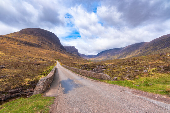 Empty applecross pass road with mountains in background under cloudy sky