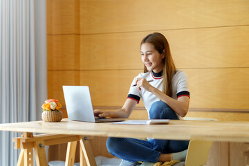 Smiling young beautiful Asian woman sitting working laptop computer at home.