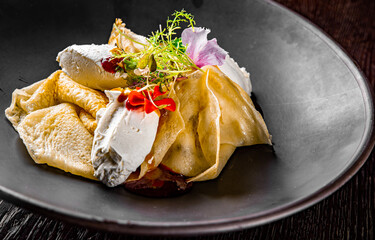 Crepes with strawberries jam and cream cheese on black plate on wooden table dark background