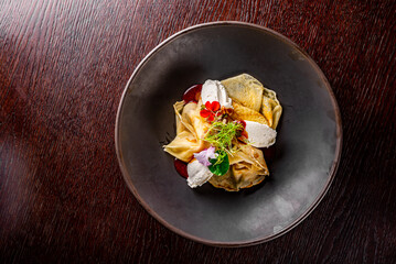 Crepes with strawberries jam and cream cheese on black plate on wooden table dark background