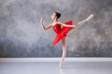 A cute little girl dreams of becoming a professional ballerina. A girl in a bright red tutu on pointe shoes dances in the hall. Vocational school student. - obrazy, fototapety, plakaty