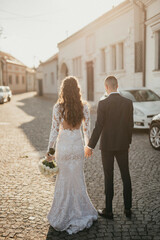 Wedding couple walking. The bride and groom holding hands.  The bride holds a bouquet in her hand.