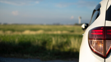 Close-up of the tail light of an white SUV while traveling on a road trip. Overlooking the fields and vast skies on vacation.