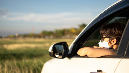 Asian tourist woman with short hair wearing a mask to prevent the spread of COVID-19, sitting in a car looking out for nature on a road trip in the concept of New Normal tourism and call for outdoor