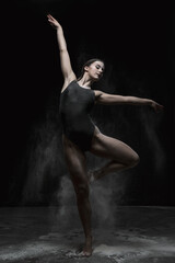 Chica joven bailando en movimiento con polvos de harina en dispersión con fondo oscuro. 
Baile y danza artística. 