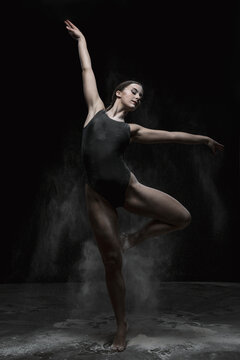 Chica joven bailando en movimiento con polvos de harina en dispersi&oacute;n con fondo oscuro. 
Baile y danza art&iacute;stica. 