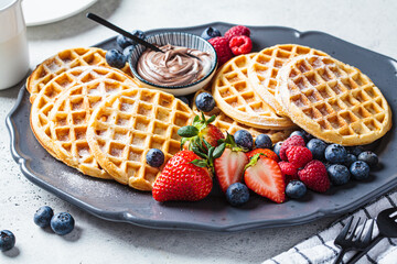 Homemade waffles with berries and chocolate cream on dark plate, gray background. Family breakfast...