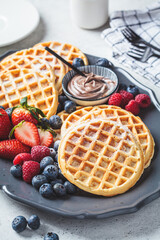 Homemade waffles with berries and chocolate cream on dark plate, gray background. Family breakfast concept.