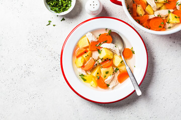 Traditional chicken soup with vegetables in white plate, gray background. Home cooking concept.