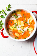 Traditional chicken soup with vegetables in red pot, gray background. Home cooking concept.