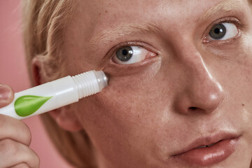 Close up of guy apply depuffing eye serum on face