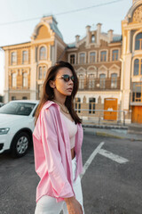 Fototapeta premium Trendy glamour woman fashion model in sunglasses with pink fashionable shirt walks in the city