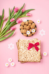 Jewish holiday Passover greeting card concept with matzah, nuts, tulip and daisy flowers on pink background.