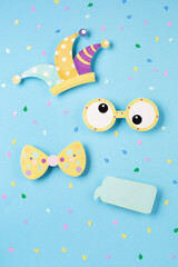 April Fool's Day holiday card with Jester hat, confetti and funny glasses on blue background, top view.