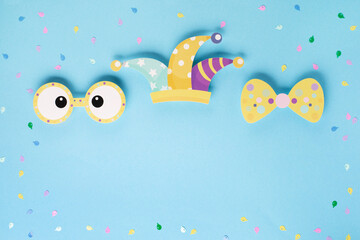 April Fool's Day holiday card with Jester hat, confetti and funny glasses on blue background, top view.