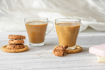 two transparent cup of coffee with milk with fresh chocolate cookies at morning shadows and sun rays through the window on gray table background. Morning coffee and breakfast concept, close up