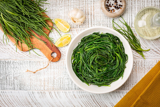 Top view of Sauteed agretti with lemon, italian food. Raw ingredient. Saltwort or salsola soda. White table.