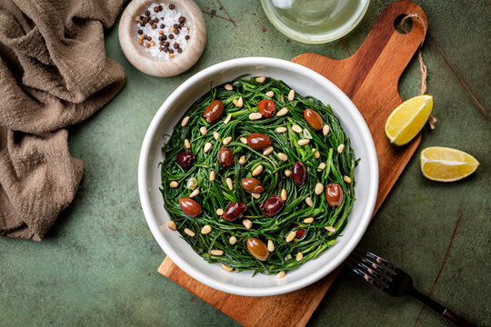 Italian Salad with Sauteed Agretti or barba di frati with garlic, Taggiasca olives, pinoli or pine nut and lemon. Salt, olive oil. Top table view. Green bacground.