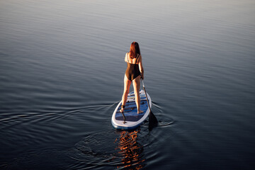 From above view on sporty middle aged woman sup boarding with oar in hands on calm blue lake water....
