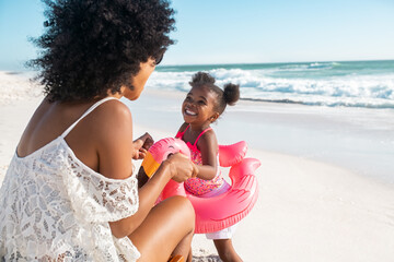 Black mother playing with inflatable flamingo with her beautiful daughter at beach