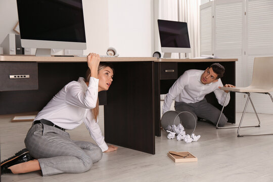 Scared employees hiding under office desks during earthquake