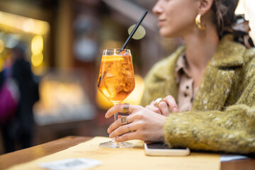 Woman holding glass with Aperol Spritz cocktail at outdoor bar, cropped view focused on drink