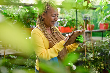 Gleeful black woman using tablet in greenhouse