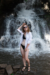 A beautiful young girl is posing near a waterfall