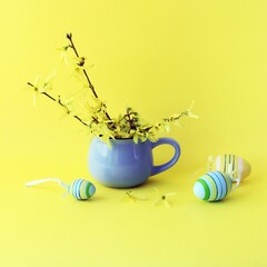 Easter eggs, fresh bouquet of first spring forsythia flowers in a blue cup on a bright yellow...