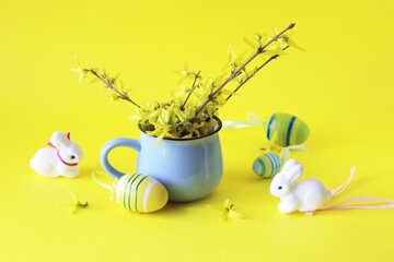 Easter eggs, fresh bouquet of first spring forsythia flowers in a blue cup on a bright yellow background