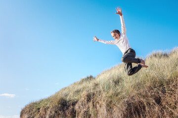 Boy running and jumping over sand dunes on beach vacation background
