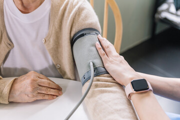 Close up nurse hand measuring blood pressure of senior woman with care. Caregiver visit at home....