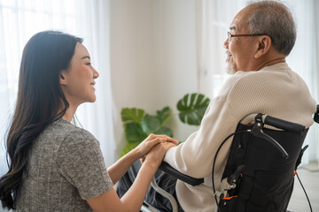 Asian daughter support old disabled man sitting on wheelchair at home. 