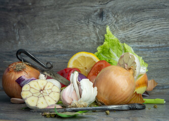 Warzywa i owoce takie jak cebula, czosnek, papryka, cytryna, sałata, pomidor na drewnianym tle.