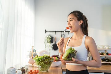 Asian attractive sport woman holding salad bowl and eat vegetables. 