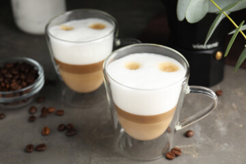 Glass cups of delicious latte macchiato and scattered coffee beans on grey table