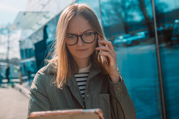 Portrait of Serious European blonde 30s businesswoman talking with phone near the office building outdooors