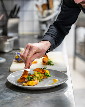 Le chef d'un restaurant finit de préparer une assiette colorée avec du saumon, de l'avocat et de la mangue