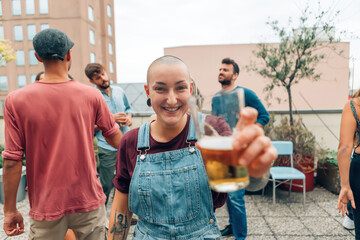 smiling skinhead gender woman cheering with a beer at the rooftop party