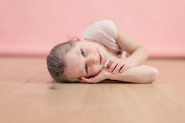 portrait of a smiling and happy caucasian little girl lying on the parquet over pink background