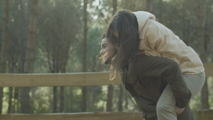Lovely young couple walking in park on sunny autumn day. Happy bearded guy carrying playful girlfriend on his back while couple having fun outdoors together. Romance, love concept