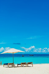 Wooden deck chairs on a sandy beach in front of ocean with boats, Zanzibar Tanzania